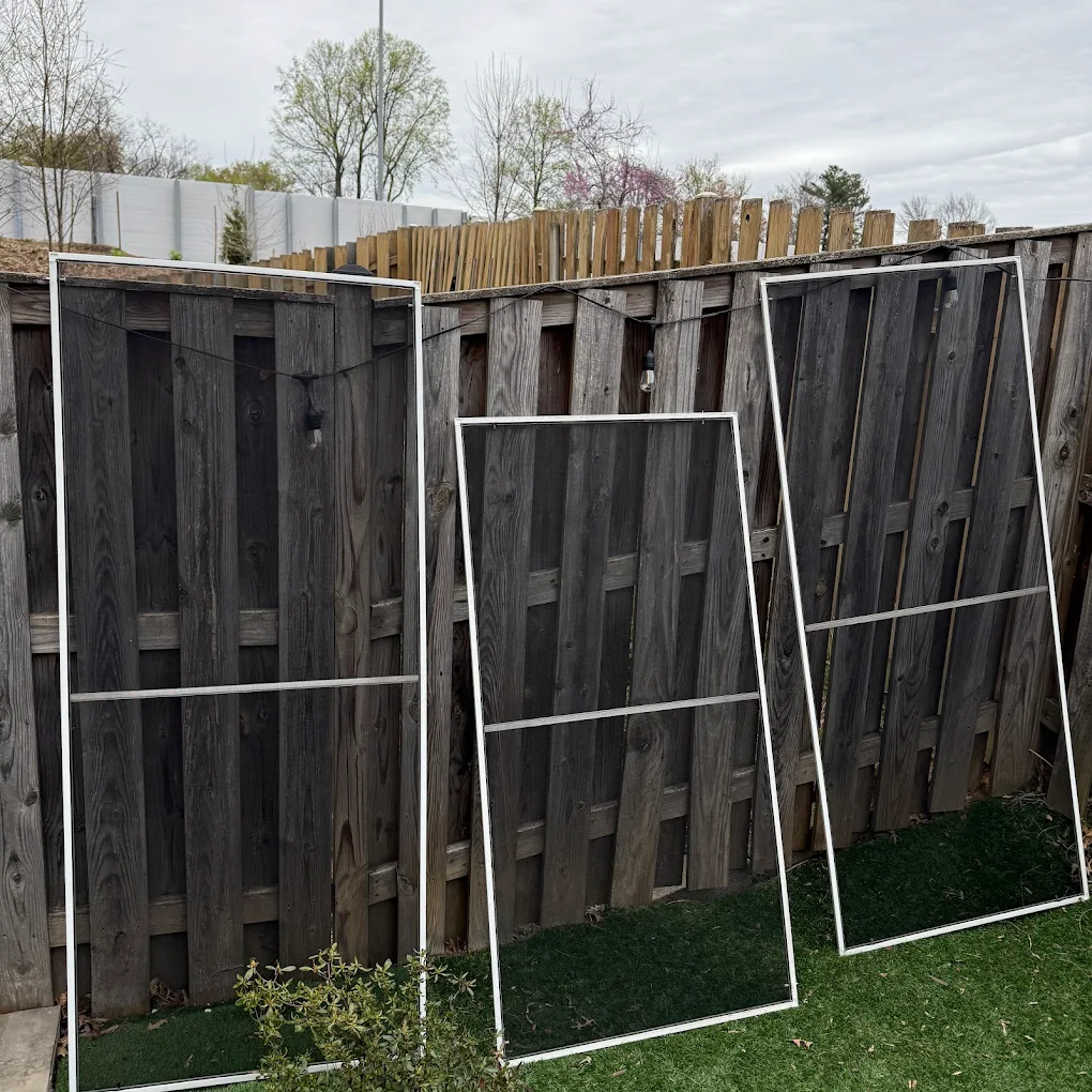 Three repaired window screen frames leaning against a backyard fence