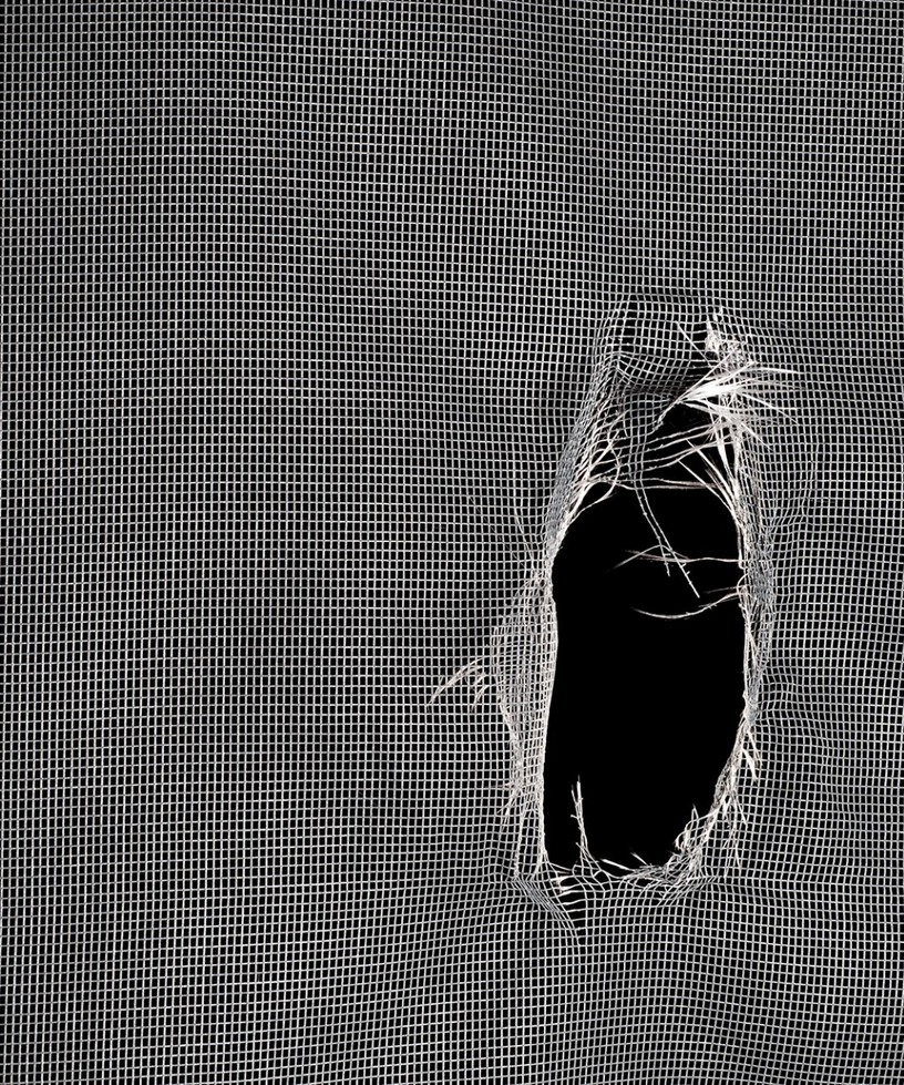 Close-up of a torn hole in window screen mesh